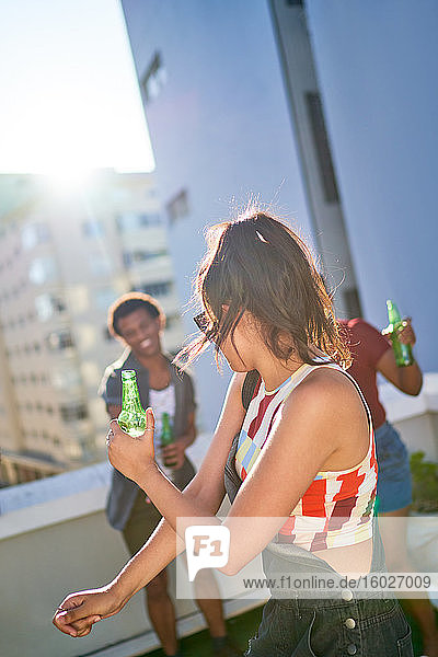 Junge Frau tanzt mit Bier auf dem sonnigen städtischen Dachbalkon