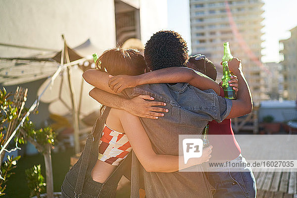 Glückliche junge Freunde umarmen sich und trinken Bier auf dem sonnigen Dach