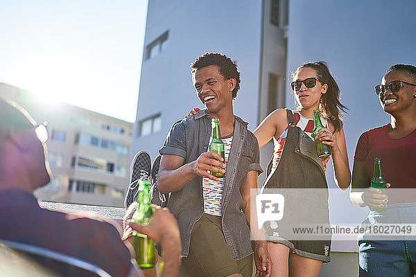 Happy young friends drinking beer on sunny urban balcony