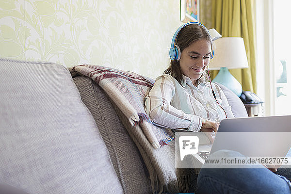Teenagerin mit Kopfhörern mit Laptop auf dem Sofa