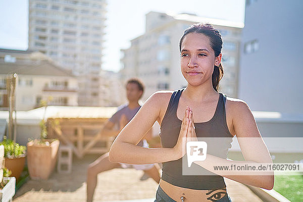 Porträt einer selbstbewussten jungen Frau  die auf einem sonnigen Dach Yoga praktiziert