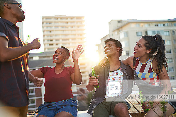 Happy young friends drinking beer hanging out on sunny urban rooftop