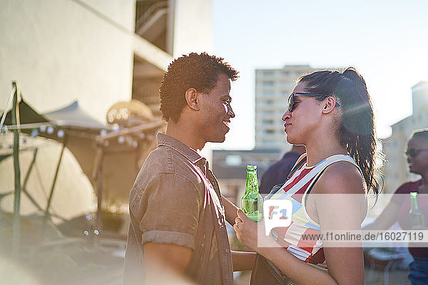 Happy young couple drinking beer and talking on sunny urban rooftop