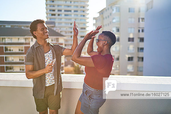 Glückliches junges Paar auf sonnigem städtischen Dachbalkon