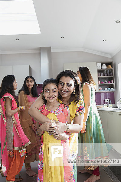 Porträt einer glücklichen indischen Mutter und Tochter in Saris  die sich in der Küche umarmen