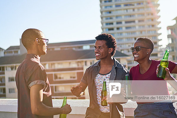 Junge Freunde unterhalten sich und trinken Bier auf dem sonnigen Balkon auf dem Dach der Stadt
