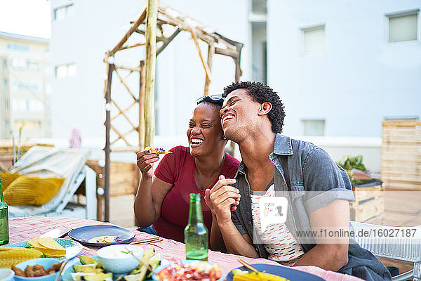 Glückliches junges Paar lacht und isst am Terrassentisch