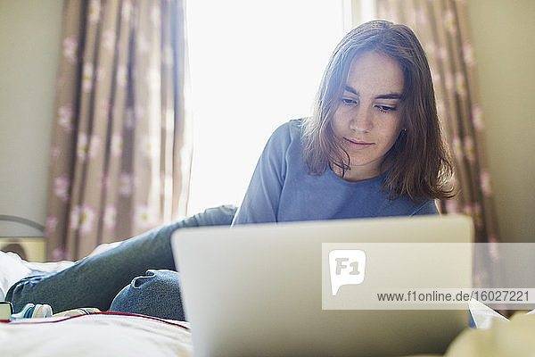 Teenager-Mädchen benutzt Laptop auf dem Bett im sonnigen Schlafzimmer