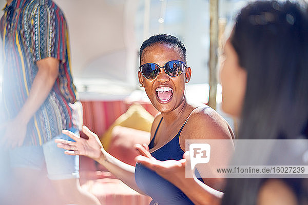 Glückliche junge Frau lacht mit Freunden auf sonniger Terrasse