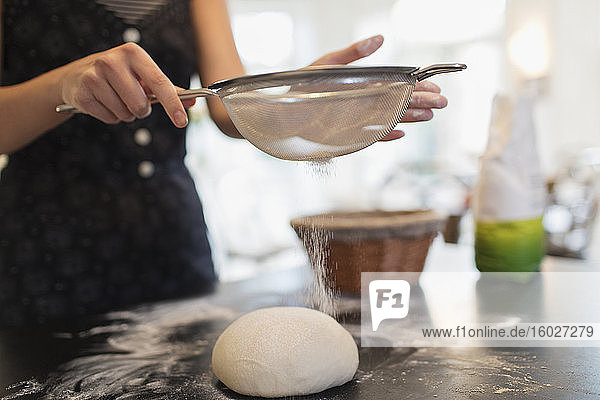 Nahaufnahme einer Frau  die Mehl aus Brotteig auf der Küchentheke sichtet