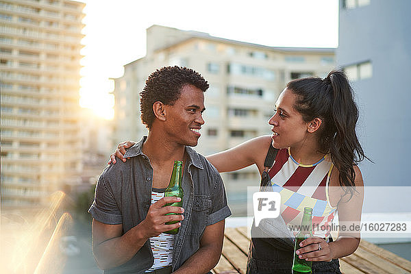 Happy young couple drinking beer on sunny urban rooftop balcony