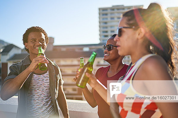 Happy young friends drinking beer on sunny urban rooftop balcony