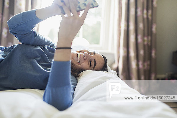 Glückliches Teenager-Mädchen benutzt Smartphone im Bett