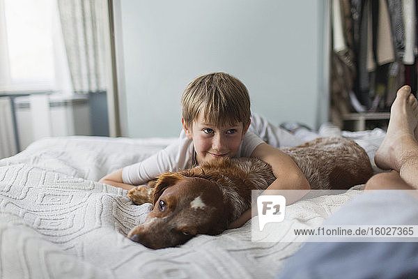 Süßer Junge kuschelt mit Hund auf dem Bett