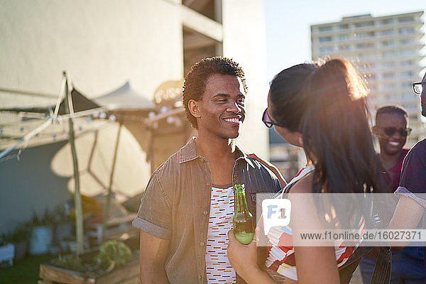 Happy young couple drinking beer on sunny urban rooftop