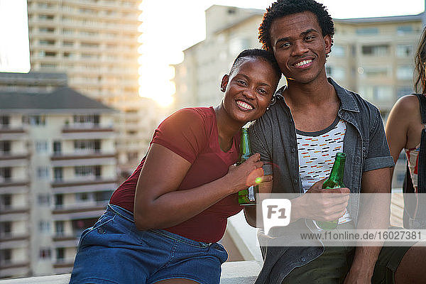 Porträt eines glücklichen jungen Paares beim Biertrinken auf dem Dach einer Stadt