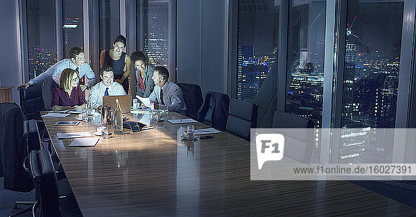 Business people working at laptop in conference room at night