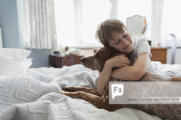 Cute boy hugging dog on bed
