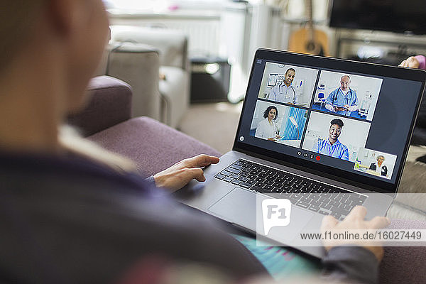 Frau mit Laptop im Video-Chat mit Ärzten vom Sofa aus