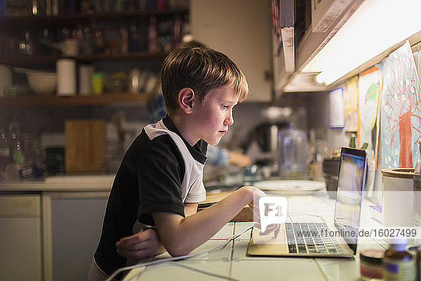 Junge macht Hausaufgaben am Laptop auf der Küchentheke