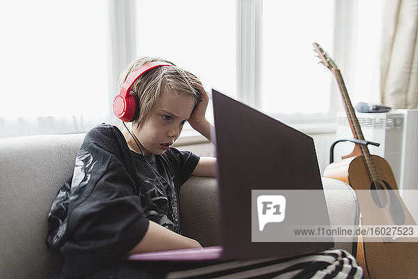 Junge mit Kopfhörer und Laptop auf Wohnzimmersofa