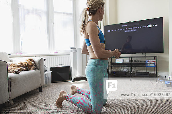 Frau praktiziert Online-Yoga am Fernseher im Wohnzimmer