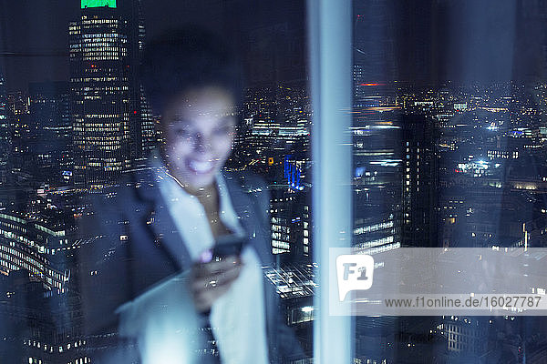 Lächelnde Geschäftsfrau überprüft Handy im Stadtfenster