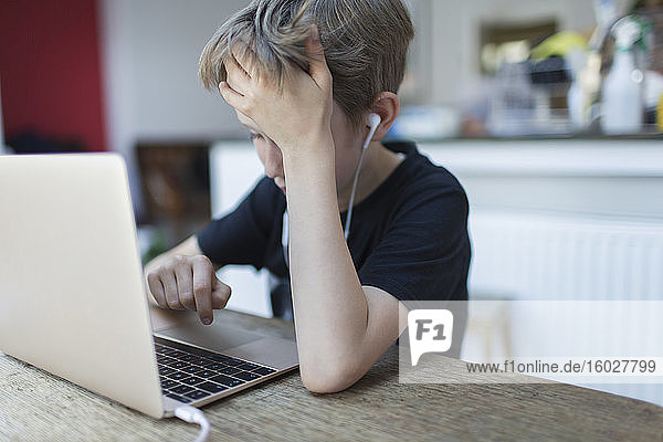 Frustrierter Junge mit Kopfhörern beim Heimunterricht am Laptop