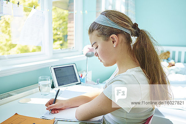 Fokussiertes Mädchen macht Hausaufgaben am Schreibtisch im Schlafzimmer