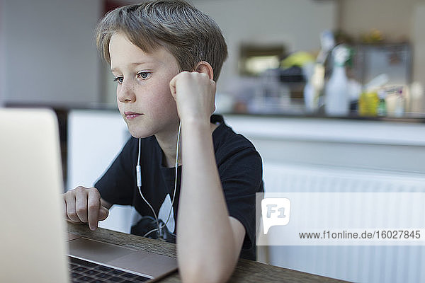 Fokussierter Junge mit Kopfhörern beim Heimunterricht am Laptop