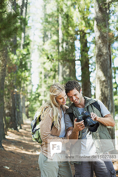 Lächelndes Paar schaut auf Digitalkamera im Wald