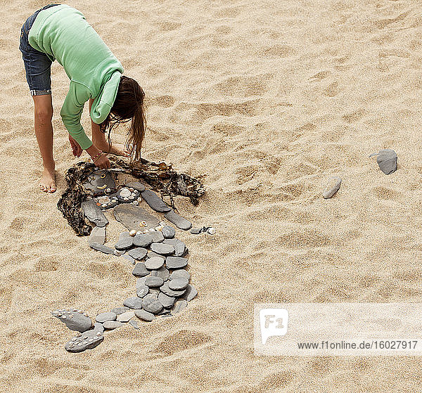 Mädchen macht Meerjungfrau aus Felsen und Algen am Strand