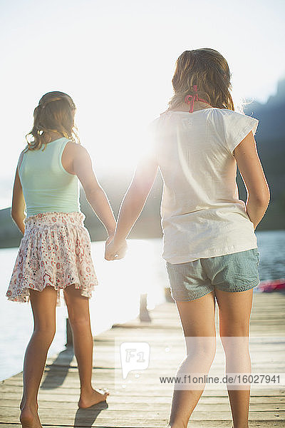 Sisters holding hands on dock over lake