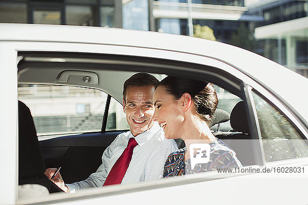 Businessman and businesswoman talking in back seat of car