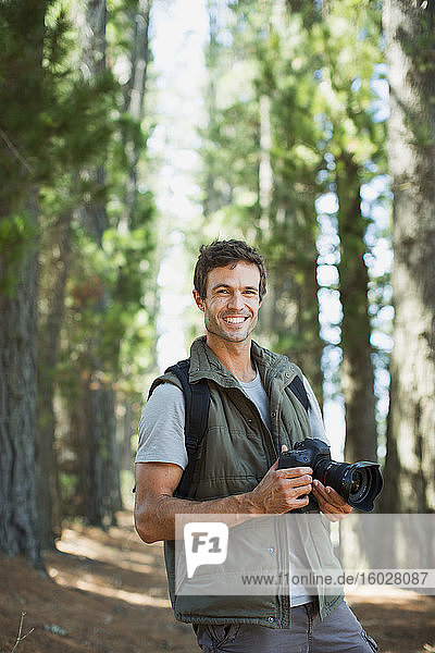 Lächelnder Mann mit Digitalkamera im Wald