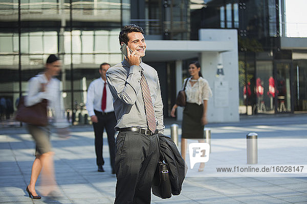 Lächelnder Geschäftsmann telefoniert mit einem Mobiltelefon vor einem städtischen Gebäude