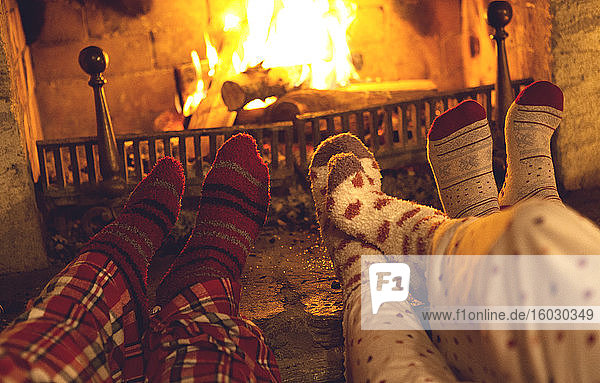 Beine und Füße von drei Personen in Pyjamas und warmen Socken  die vor einem Kamin liegen.