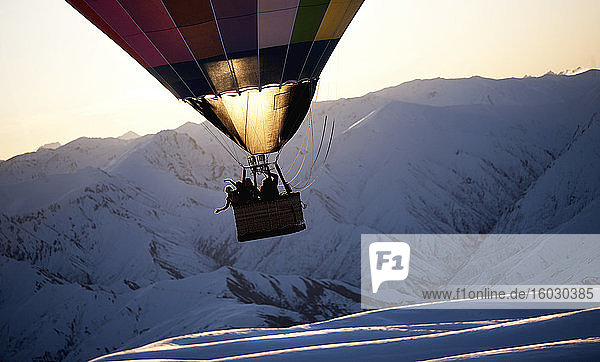 Menschen in einem Heißluftballon mitten in der Luft über einem schneebedeckten Berg.