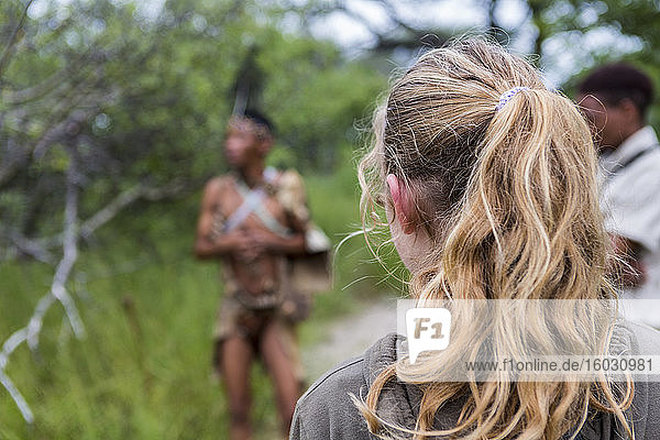 Rückansicht eines jugendlichen Mädchens  das mit einer Gruppe von Buschmännern aus dem Volk der San unterwegs ist.