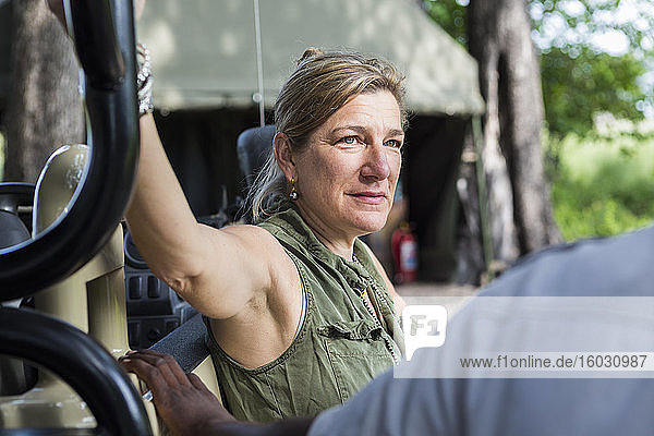 Porträt einer erwachsenen Frau  die sich auf ein Safari-Fahrzeug lehnt  Zeltlager  Botswana