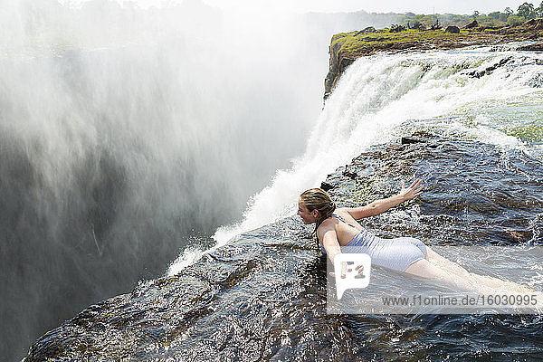 Young girl in the water at the Devils Pool lying on her front  arms spread out  at the edge of the cliff of Victoria Falls.