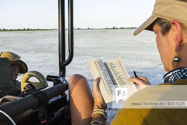 Eine Frau betrachtet ein Buch oder eine Zeitschrift in einem Safari-Fahrzeug  Botswana