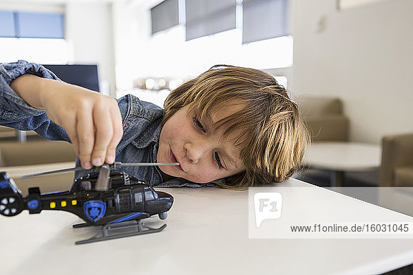 A five year old boy playing with a toy tractor on a table in an airport departure lounge.
