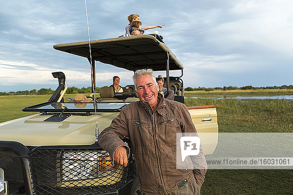 Ein lächelnder Safari-Führer und eine Familie von Touristen in einem Safari-Fahrzeug.