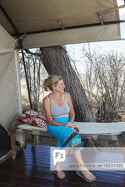 Eine reife Frau sitzt unter einer Plane an einem Zelt in einem Wildreservatscamp.