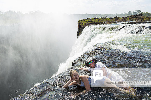 Man and a girl  father and daughter in the water of the Devil's Pool on the edge of Victoria Falls  mist rising from the falling water.