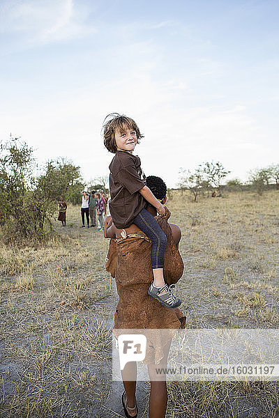 Fünfjähriger Junge  der auf den Schultern eines San-Buschmanns reitet.