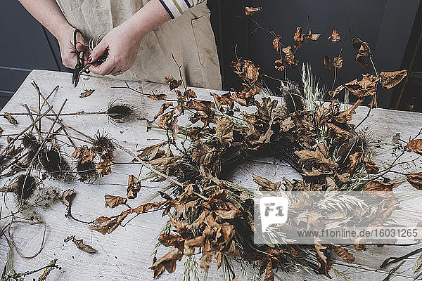Woman making a small winter wreath of dried plants  brown leaves and twigs  and seedheads.