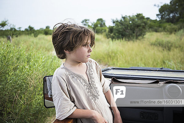 Sechsjähriger Junge der in einem Safari-Jeep steht und sich in der Landschaft umsieht.