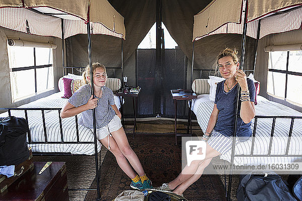 Unterkunft in einem Wildreservatscamp  Mutter und Tochter auf Betten sitzend in einem Zelt.
